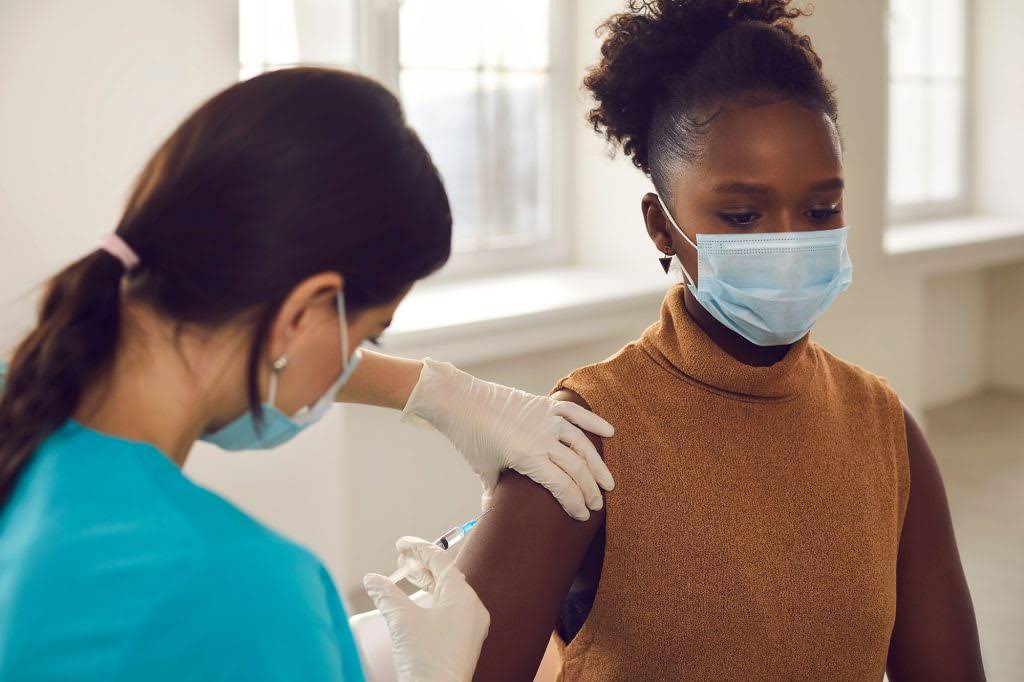 African american woman patient in protective face mask sitting getting vaccination injection